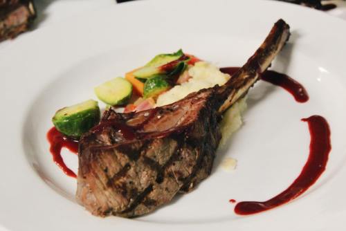 A beautifully plated lamb chop with a red sauce, served with mashed potatoes and colorful vegetables.