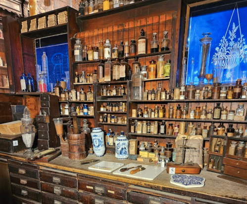 A vintage apothecary display with shelves of glass bottles, jars, and wooden drawers, showcasing historical medicinal items.