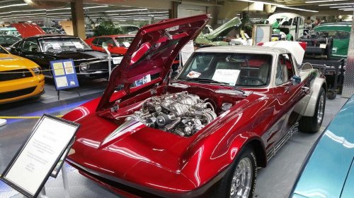 A red vintage car with the hood open, showcasing a detailed engine, displayed in a car museum.
