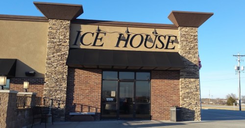 Exterior of a building with a sign that reads "ICE HOUSE," featuring stone accents and a clear blue sky.