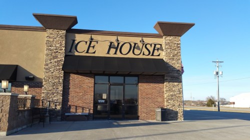 Exterior of a building with a sign that reads "ICE HOUSE," featuring stone accents and a clear blue sky.