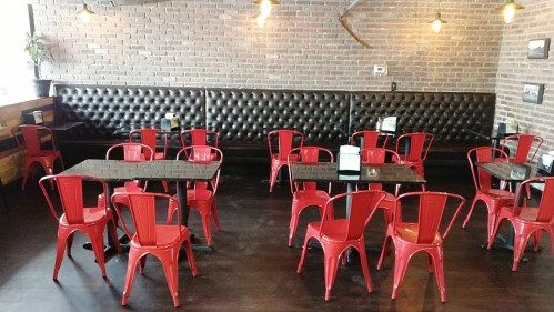 A cozy restaurant interior featuring red metal chairs and black tables against a brick wall.