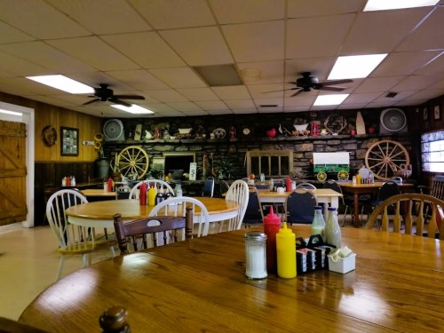 A cozy restaurant interior with wooden tables, chairs, and a stone wall featuring decor and condiments on the tables.