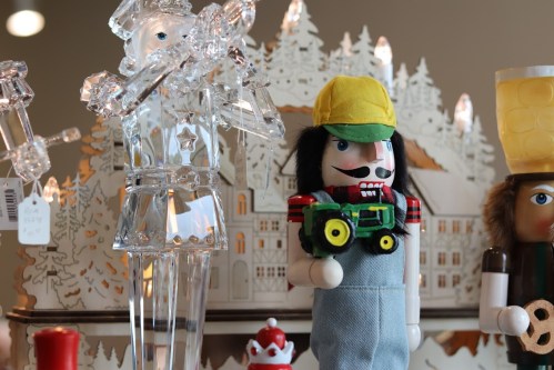 A colorful display of nutcracker figurines, including one holding a toy tractor, set against a festive backdrop.