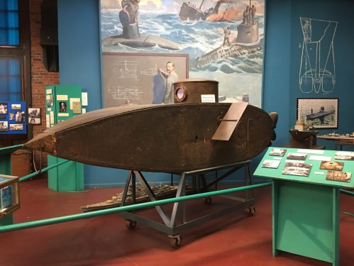 A historical submarine exhibit in a museum, featuring a model and informational displays on the walls.