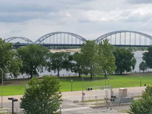 A view of a river with a bridge in the background, framed by green trees and a grassy area.