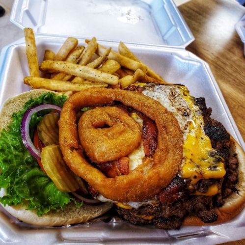 A hearty burger topped with cheese, bacon, an onion ring, lettuce, and pickles, served with a side of fries.