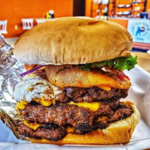 A towering burger with multiple beef patties, melted cheese, lettuce, bacon, and a fried egg, all in a soft bun.