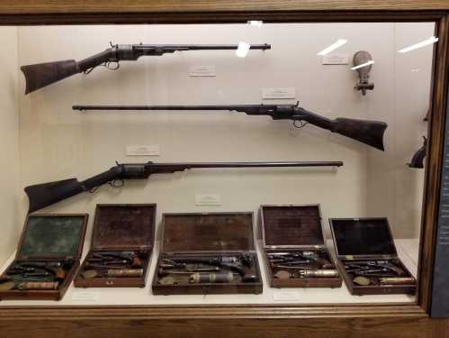 Display case featuring vintage rifles and pistols, showcasing various firearms and their wooden cases.