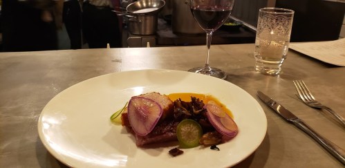 A plated dish featuring meat, colorful vegetables, and a glass of red wine on a table.
