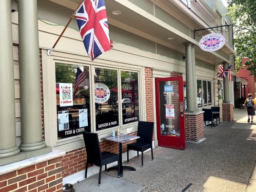 Exterior of a British-themed restaurant with flags, featuring outdoor seating and a sign for fish and chips.