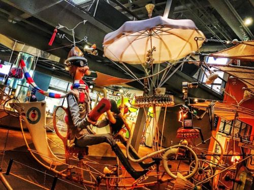 A whimsical sculpture of a character in a contraption, featuring a parasol and various mechanical elements.