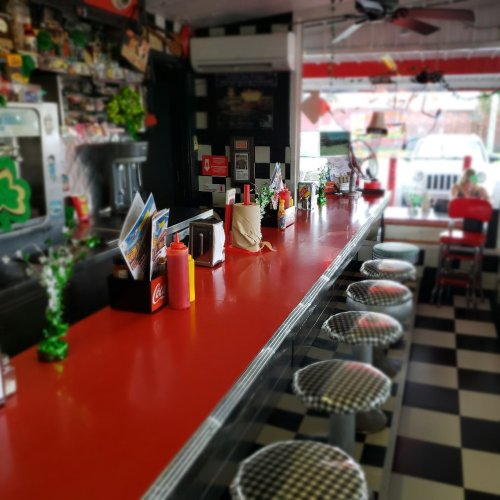 A retro diner interior with a red counter, checkered stools, and colorful decor, creating a nostalgic atmosphere.