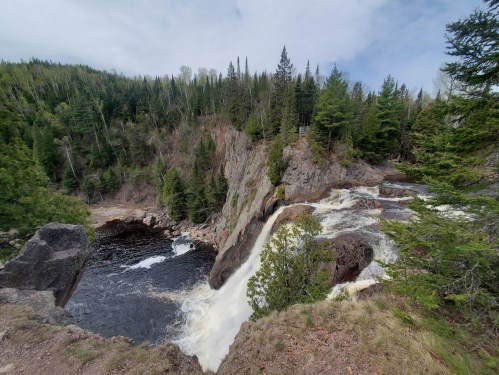 A scenic view of a waterfall cascading into a river, surrounded by lush green trees and rocky cliffs.