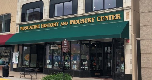 Exterior of the Muscatine History and Industry Center, featuring a green awning and large windows displaying a gift shop.