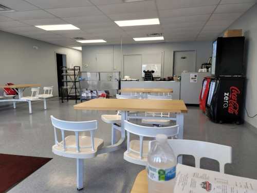 A clean, empty dining area with tables and chairs, featuring a Coca-Cola vending machine and a menu on the table.