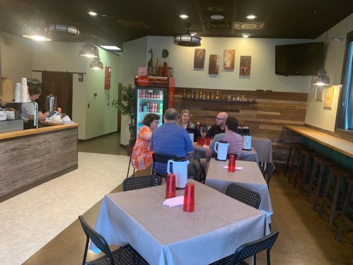 A cozy restaurant interior with a group of people dining at a table, featuring wooden decor and red drink dispensers.