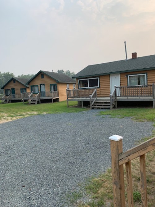 A row of wooden cabins with porches, set on a grassy area with gravel, under a hazy sky.
