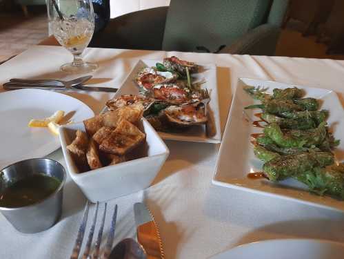 A table setting with two plates of appetizers: grilled seafood and stuffed peppers, alongside a bowl of chips and a drink.