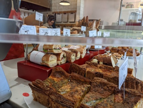 A display case filled with various sandwiches and baked goods, including quiches and pastries.
