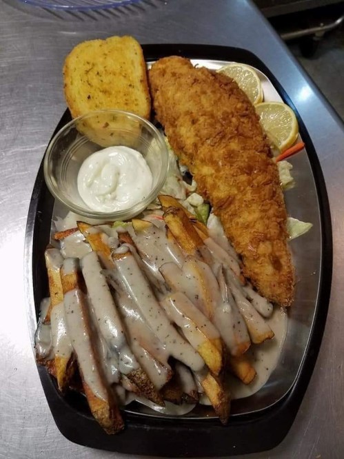A plate with fried fish, seasoned fries topped with gravy, a side of coleslaw, and garlic bread.