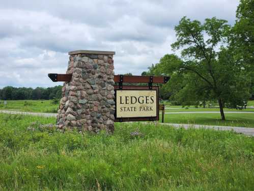 Sign for Ledges State Park, featuring a stone structure and green grass under a cloudy sky.