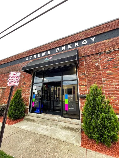 Exterior of Xtreme Energy building with a sign, large glass entrance, and landscaped shrubs. No parking sign visible.