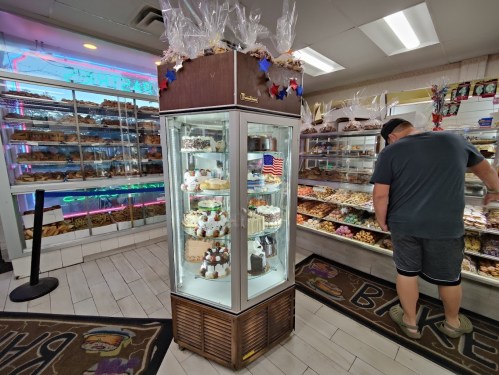 A bakery display with various pastries and desserts, featuring a customer browsing the treats.