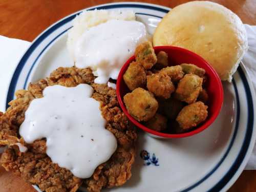 A plate featuring fried chicken with white gravy, mashed potatoes, fried okra, and a biscuit.