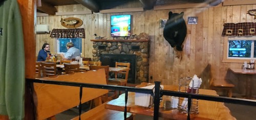 Cozy restaurant interior with wooden walls, a bear mount, and two patrons seated at a table.