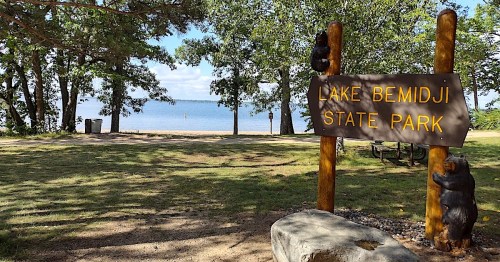 Sign for Lake Bemidji State Park with a view of the lake and trees in the background.