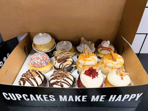 A box of assorted cupcakes, featuring various flavors and toppings, with a cheerful message on the side.