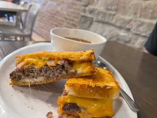 A plate with a grilled cheese sandwich filled with beef and cheese, alongside a bowl of soup.