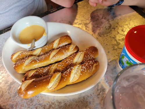 A plate of soft pretzel sticks with a small bowl of mustard for dipping, served on a textured table.