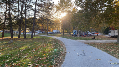 A winding path through a park with autumn leaves, leading to RVs and trees under a warm sunset.