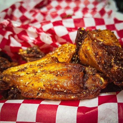 A close-up of crispy, seasoned chicken wings in a red and white checkered basket.