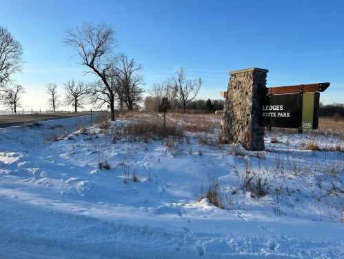 Sign for Ledges State Park beside a snowy landscape and a clear blue sky, with trees in the background.