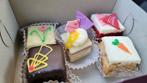 A box of assorted colorful pastries, including chocolate, cream, and fruit-topped treats.