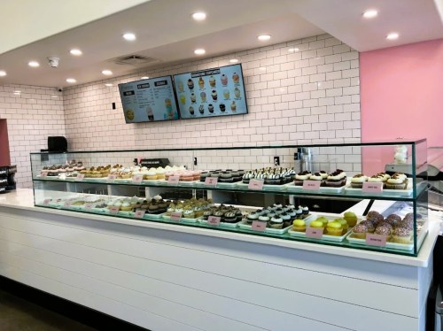 A display case filled with various colorful cupcakes and desserts in a modern bakery with a pink and white interior.