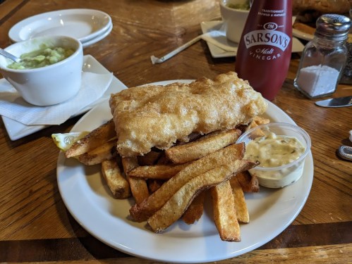 A plate of golden-battered fish and chips, served with tartar sauce, a slice of lemon, and a side of mushy peas.
