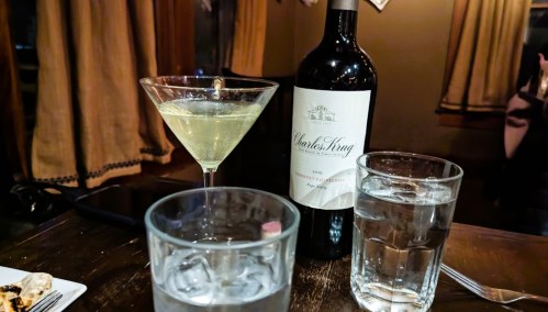 A table setting with a martini, a bottle of Charles Krug wine, and two glasses of water.