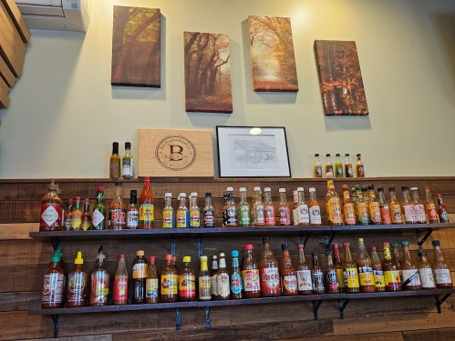 A wall display featuring various hot sauce bottles on shelves, with nature-themed artwork above.
