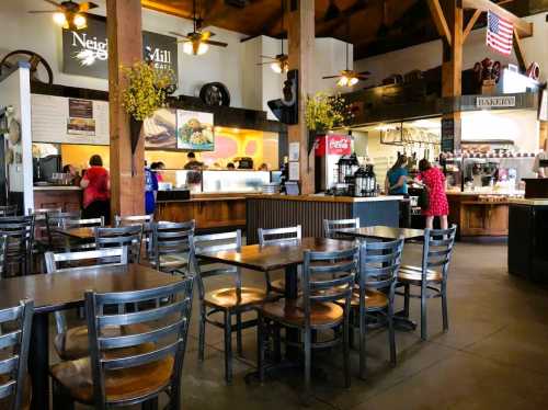 A cozy café interior with wooden beams, tables, and a counter where staff serve customers. Brightly lit and inviting atmosphere.