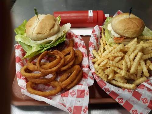 Two trays of food: one with two sandwiches on lettuce and the other with onion rings and crinkle-cut fries.