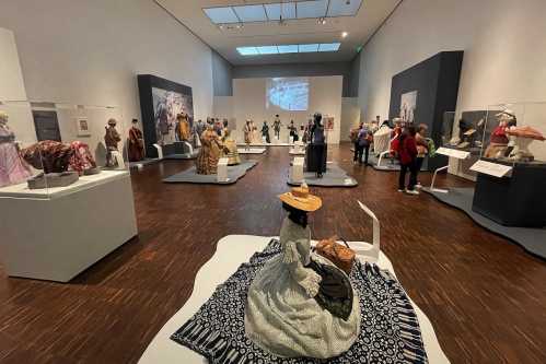 A museum exhibit featuring historical garments displayed on mannequins, with visitors exploring the space.