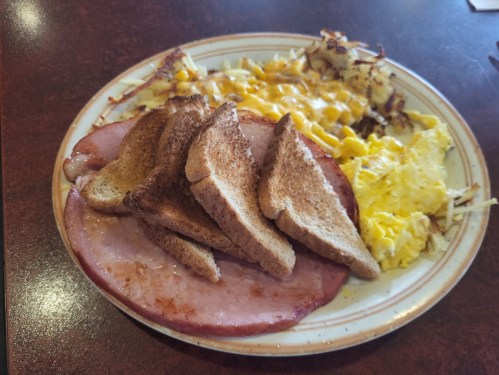A plate of breakfast featuring toast, scrambled eggs, ham, and cheesy hash browns.