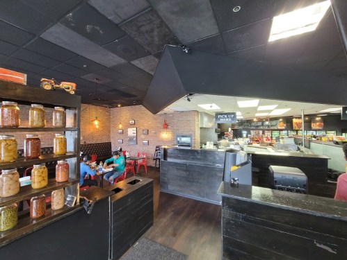 Interior of a casual restaurant featuring a counter, seating area, and jars of food on display.