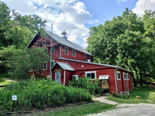 A red barn-style building surrounded by greenery and trees under a partly cloudy sky.