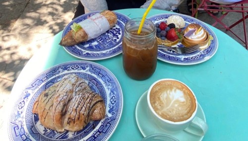 A table with a croissant, pastry, fruit tart, berries, and a cup of coffee, all set on blue patterned plates.