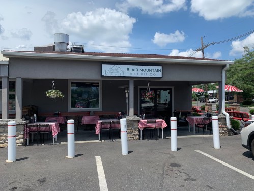 Exterior of Blair Mountain Biscuit Co. featuring outdoor seating with checkered tablecloths and a sign above the entrance.